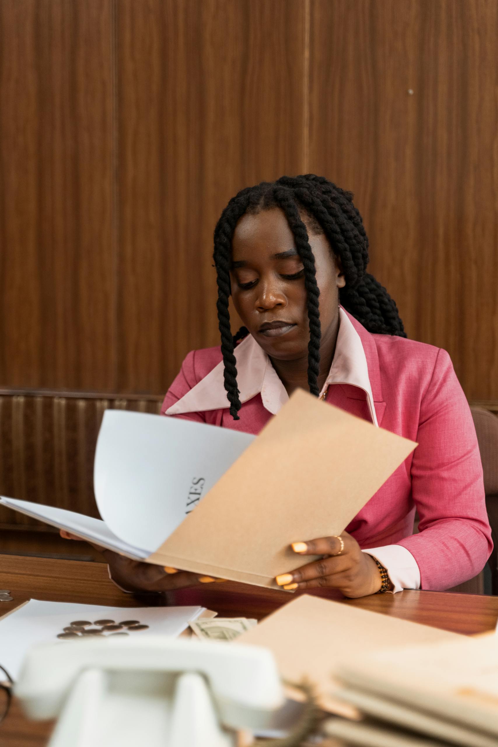 Black businesswoman in vintage attire reviewing finance documents at office desk.