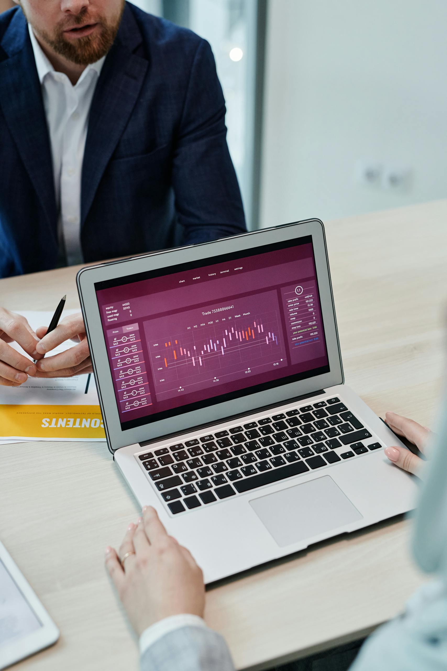 High-angle shot of business meeting with graph on laptop screen and documents on table.